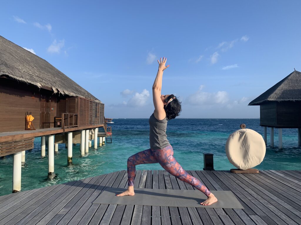 Shruthi practicing warrior pose on a beach during a yoga retreat